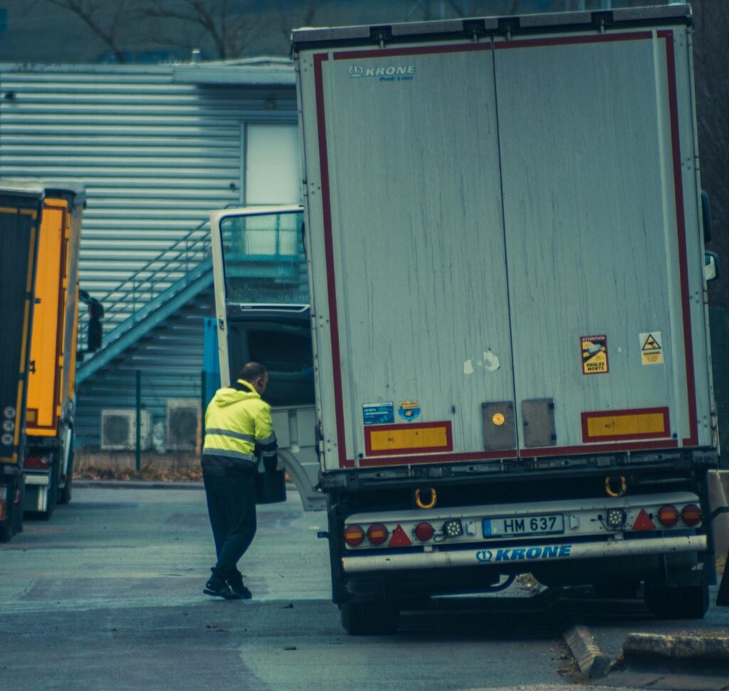 A truck driver in high-visibility gear unloading cargo at an industrial facility.